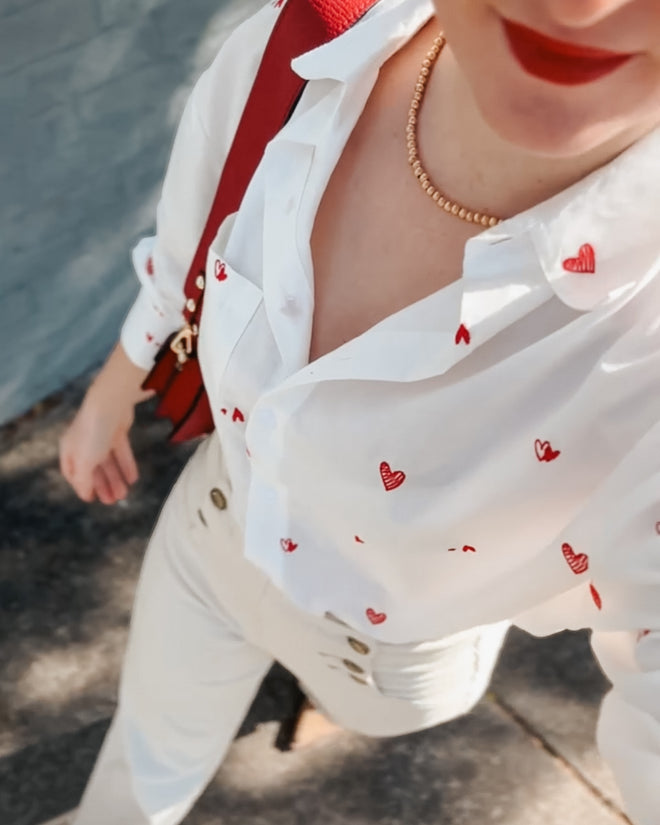 Person wearing a white blouse with red heart patterns and beige pants.
